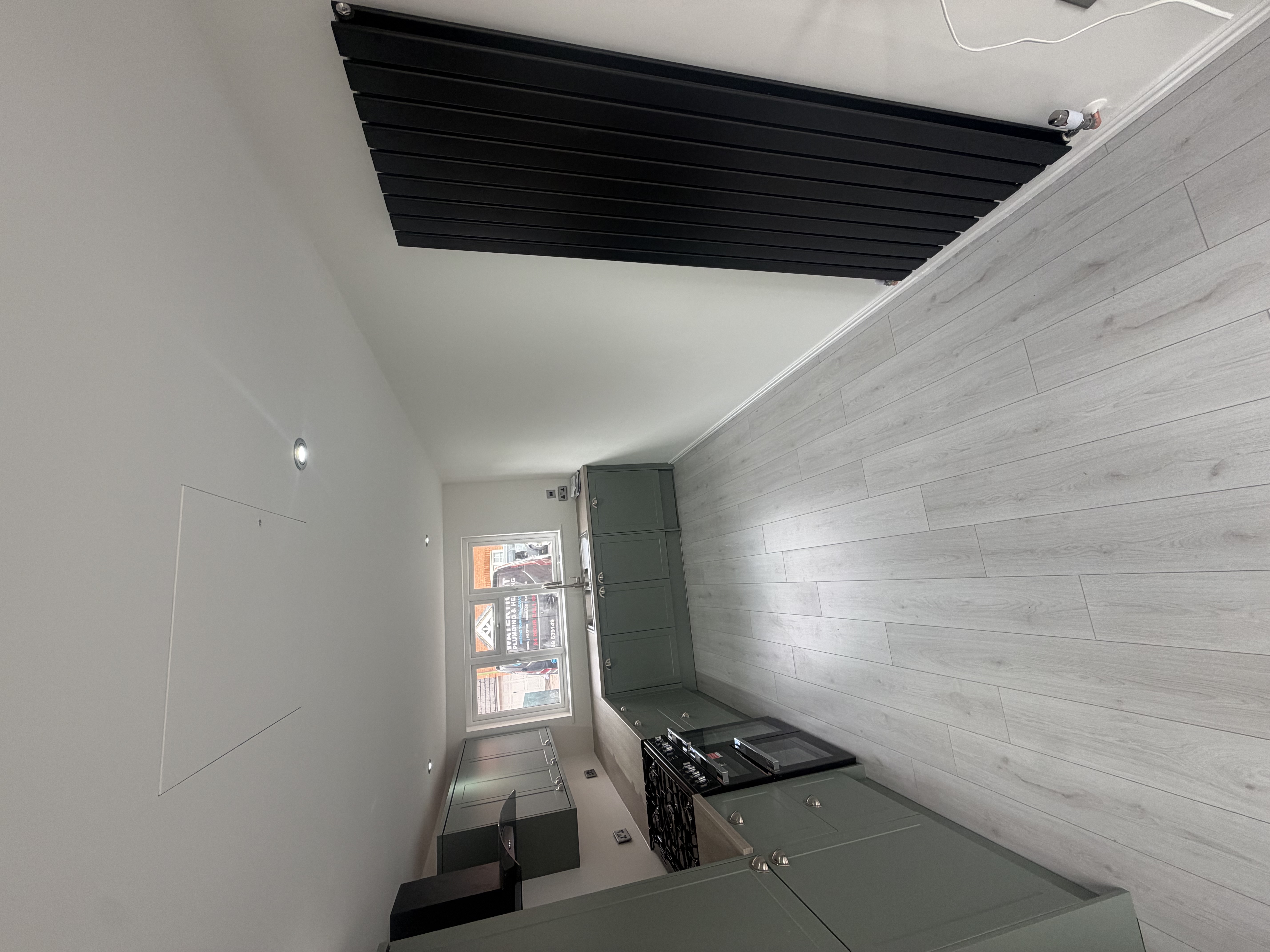 A modern kitchen with sage-green shaker units, wood-effect worktop, black range cooker and a tall black vertical designer radiator