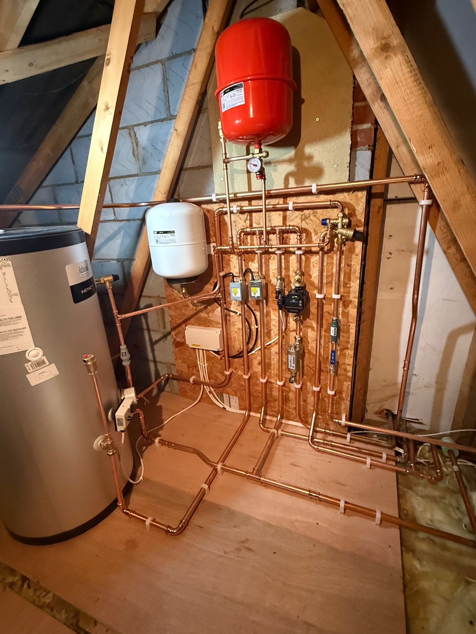 Immaculate loft heating installation with an Ideal Instinct cylinder, red and white expansion vessels, pump and precise copper pipework