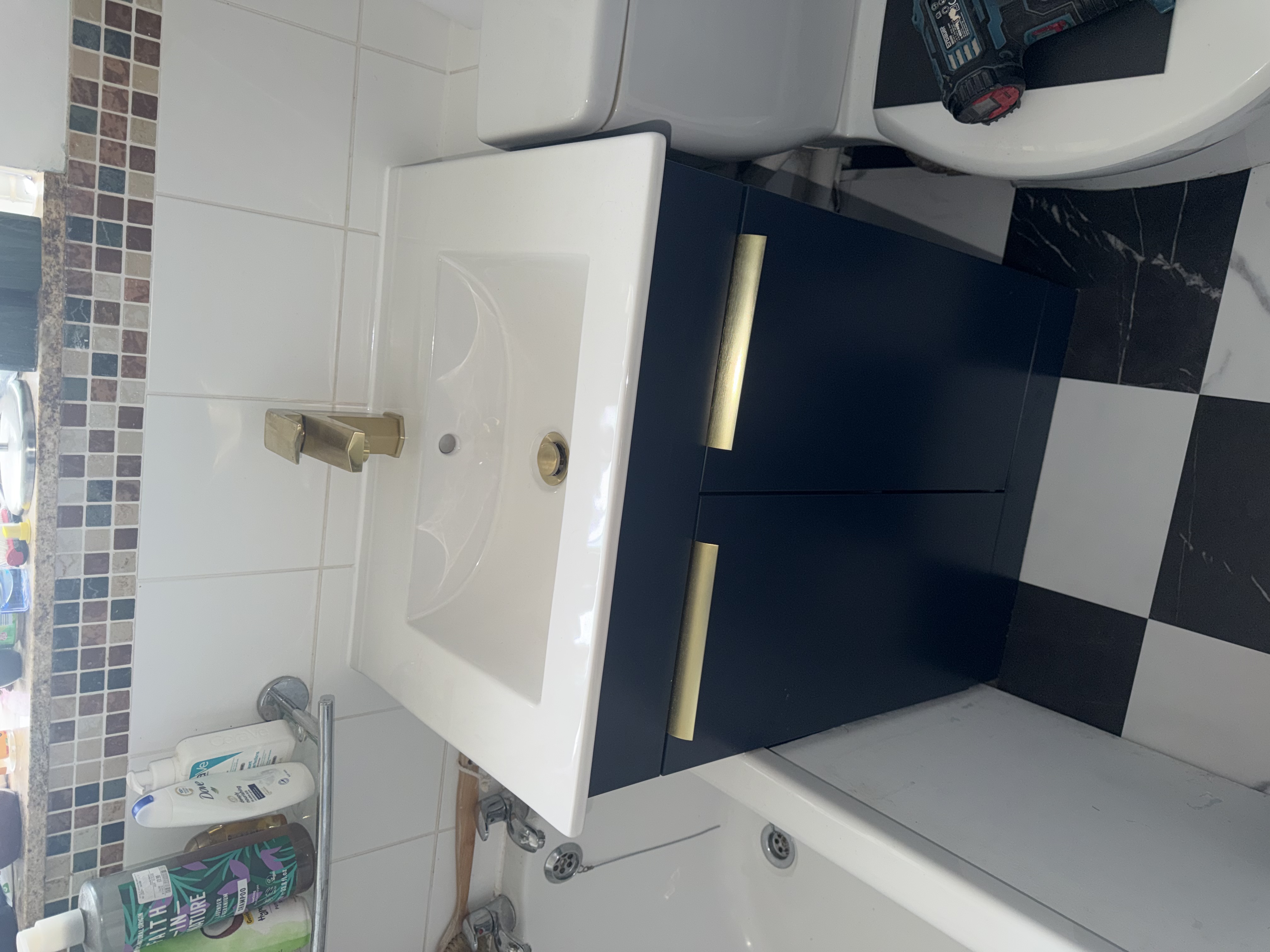 A navy blue bathroom vanity unit with brushed brass handles and matching brass mixer tap over a white basin